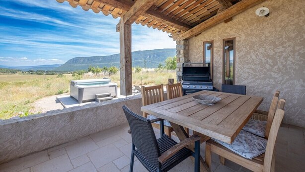 An outdoor patio with a wooden table, chairs, a grill, and a hot tub. - Holiday Home "Time-out" with Mountain Views, Shared Pool, and Wi-Fi (Laragne-Montéglin)