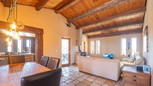A rustic interior with a wooden dining table, a white sofa, and a stone-tiled floor. - Holiday Home "Time-out" with Mountain Views, Shared Pool, and Wi-Fi (Laragne-Montéglin)