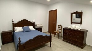 A bedroom with a wooden bed, a dresser, a chair, and a door. - Casa da Avó Bia (Penhascoso)