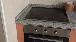 A kitchen with a black oven, a built-in stovetop, and wooden cabinets. - Casa da Avó Bia (Penhascoso)