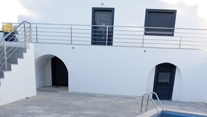 A swimming pool with a metal ladder, a white building with two doors, and a staircase leading to an upper level. - Casa da Avó Bia (Penhascoso)
