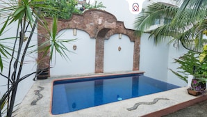 Une piscine dotée d’une terrasse carrelée, entourée de plantes et bordée d’un mur de briques agrémenté d’éléments décoratifs.