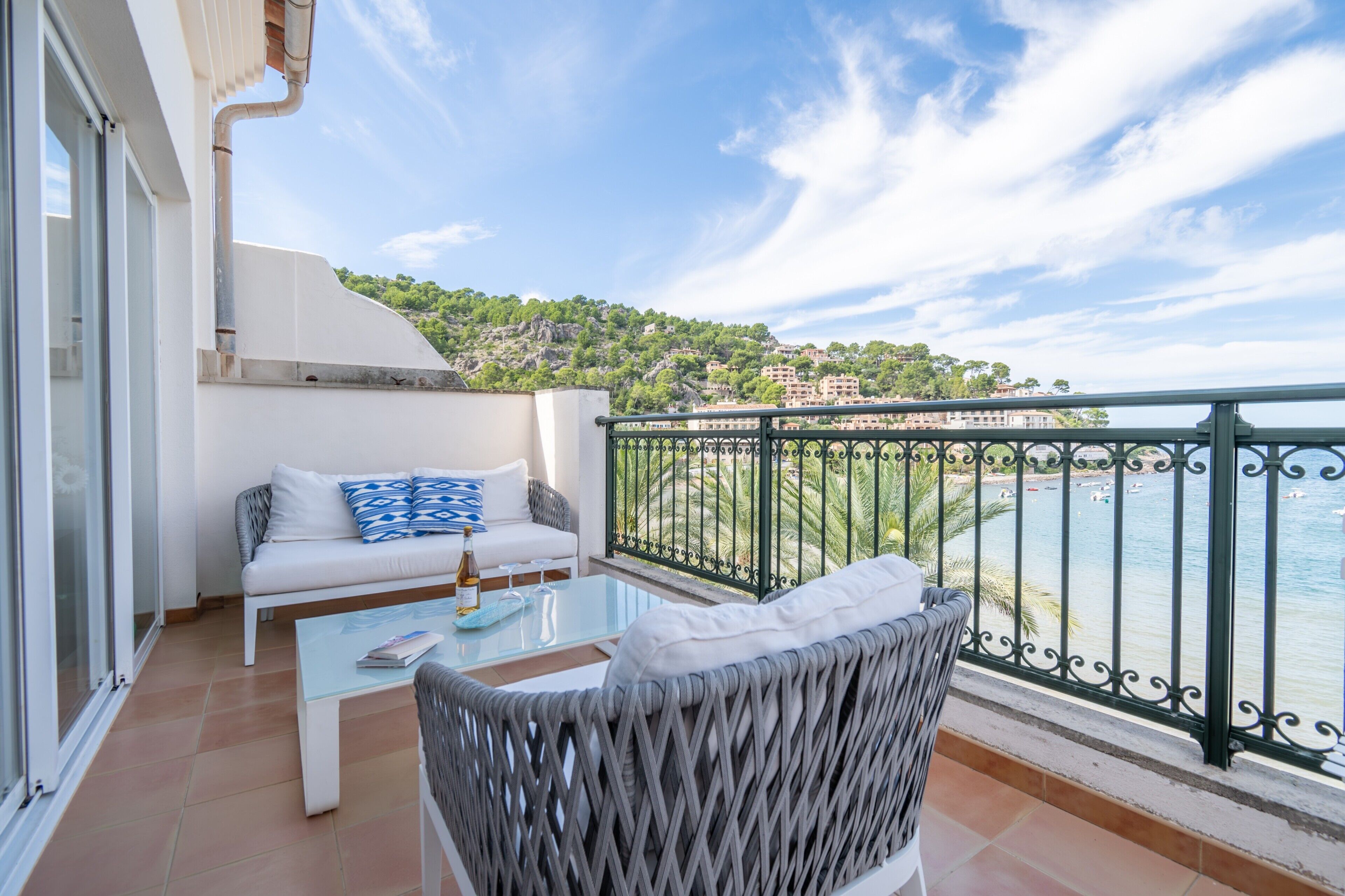 Un balcon avec un canapé blanc, une chaise en osier et une table en verre.