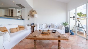 Un salón moderno con una mesa de centro de madera, un sofá blanco y un telescopio sobre un trípode.