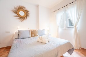 Une chambre à coucher avec un lit, des oreillers, un miroir fixé au mur et une fenêtre avec des rideaux.