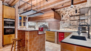 A kitchen with a brick island, wooden cabinets, a red refrigerator, and a hanging rack. - Holiday Home 'Masia Can Divi' with Mountain Views, Wi-Fi and Air Conditioning (Ametlla del Valles)