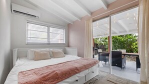 A bedroom with a large bed, a window, and a sliding glass door leading to an outdoor area with furniture.