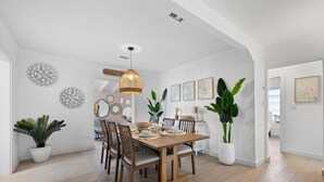 A dining area with a wooden table, chairs, a hanging light fixture, and potted plants.