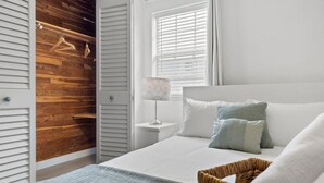 A bedroom with a bed, a nightstand, a lamp, a wooden closet, and a window with blinds.