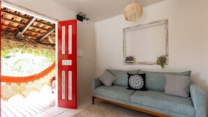 Una habitación con un sofá azul claro, una puerta roja, una cesta trenzada colgando del techo y un espejo enmarcado en la pared.