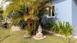 Un jardín con una estatua, palmeras y una casa de fachada azul.