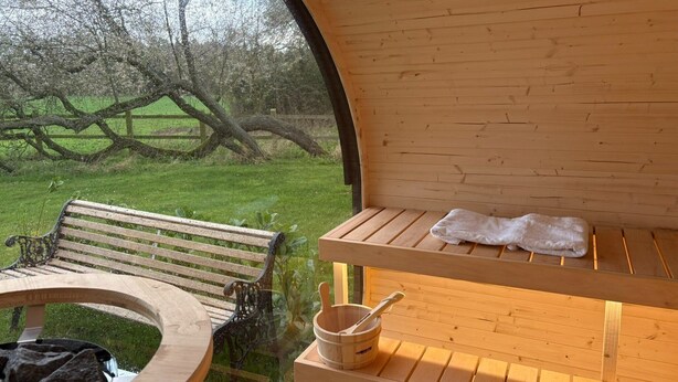 Una sauna de madera con bancos, una mesa, una toalla y un cubo con una cuchara.