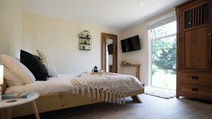 Un dormitorio con cama de madera, una mesita de noche pequeña, televisor montado en la pared y un ventanal grande.