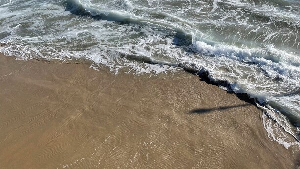 A beach with waves crashing onto the shore and a clear blue sky.