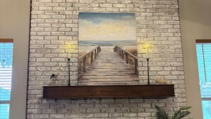 A fireplace with a brick wall, a painting of a beach, and a wooden bench.