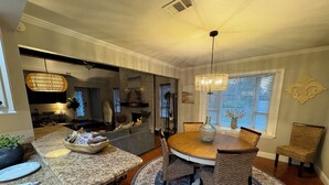 A dining area with a round table, woven chairs, a patterned rug, and a chandelier.