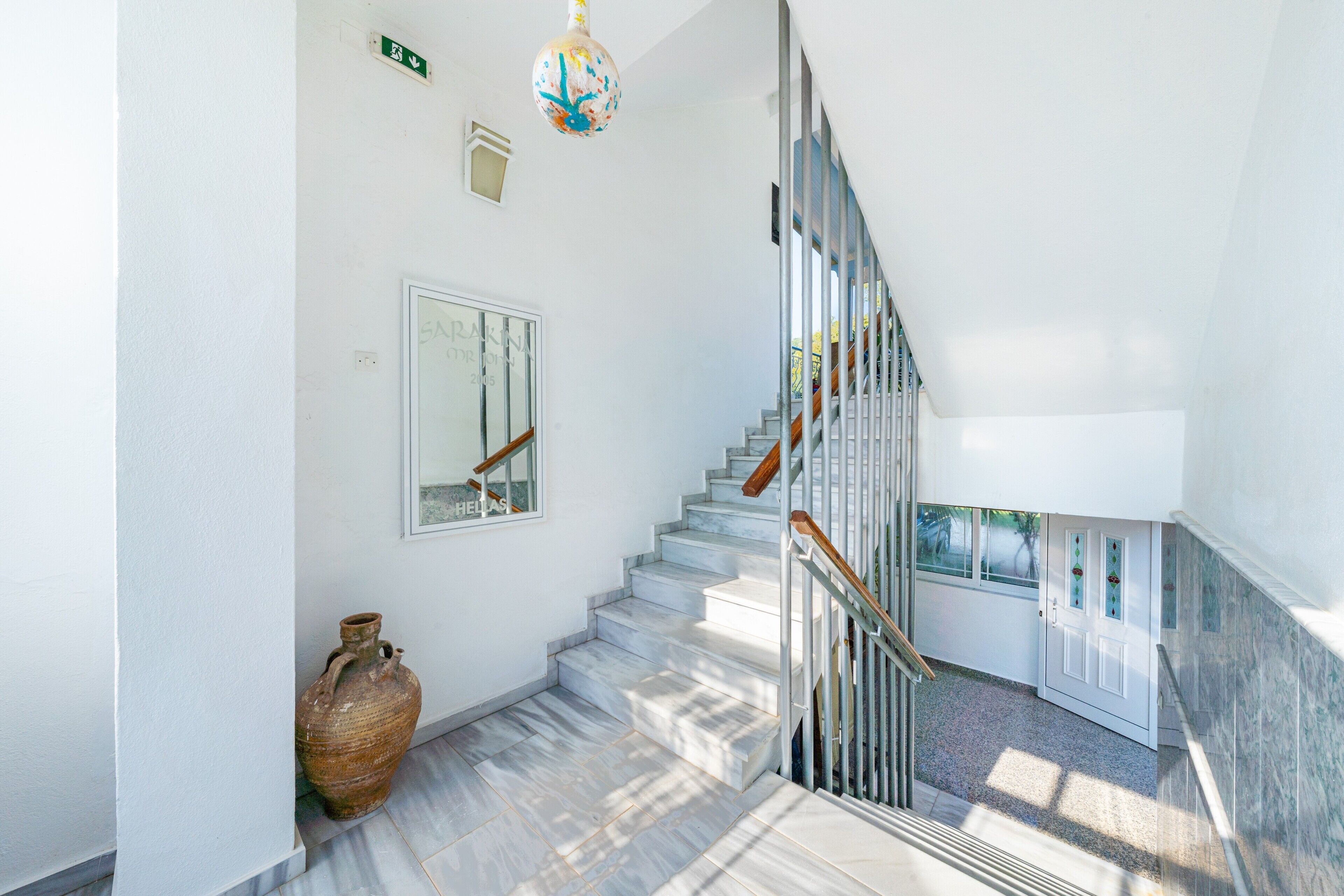 Una escalera con una pared blanca, un jarrón grande y una lámpara esférica.