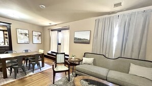 A living room with a dining table, chairs, a sofa, a coffee table, and artwork on the walls.