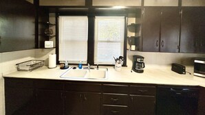 A kitchen with dark cabinets, a white countertop, a sink, a coffee maker, and a window with blinds.