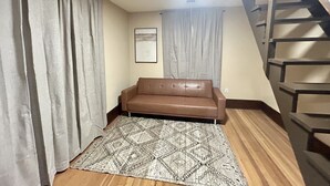 A living room with a brown sofa, a patterned rug, a staircase, and a framed picture on the wall.