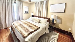 A hotel room with a bed, a ceiling fan, a bedside table with a lamp, and a framed picture on the wall.