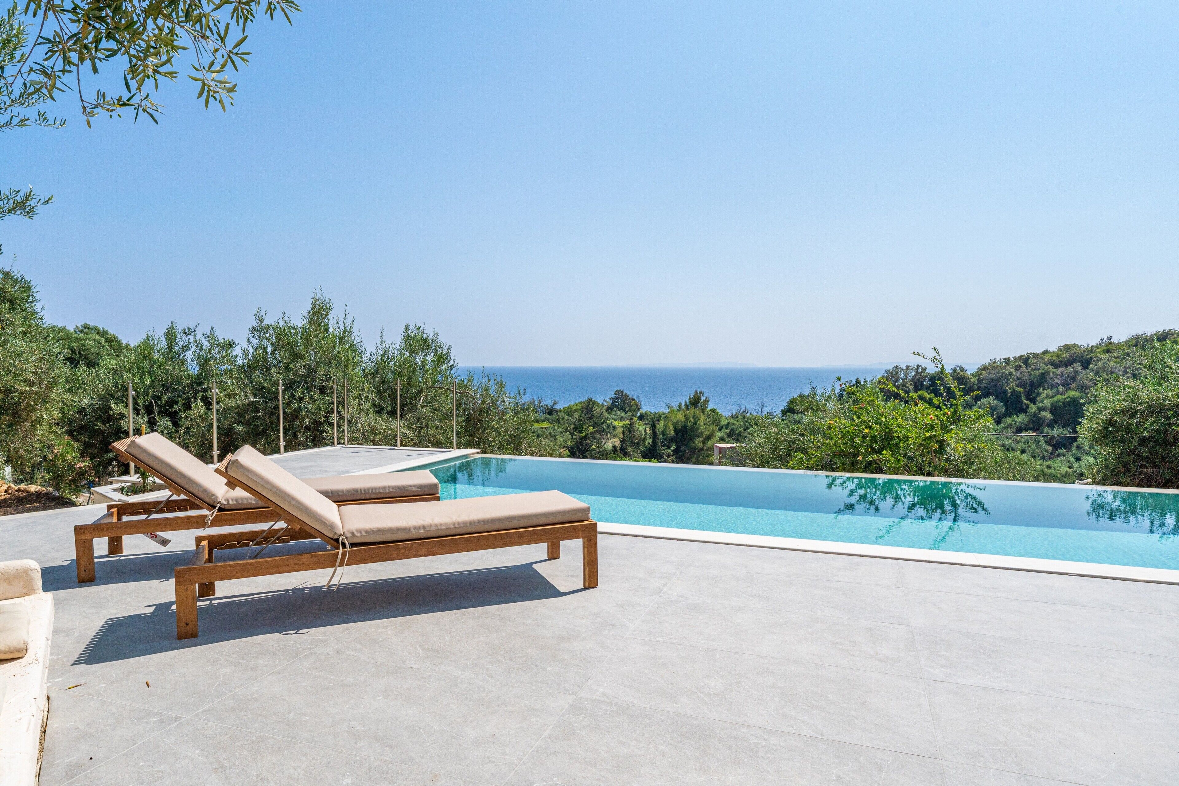 Piscina com espreguiçadeiras, cercada por vegetação e vista para o mar.