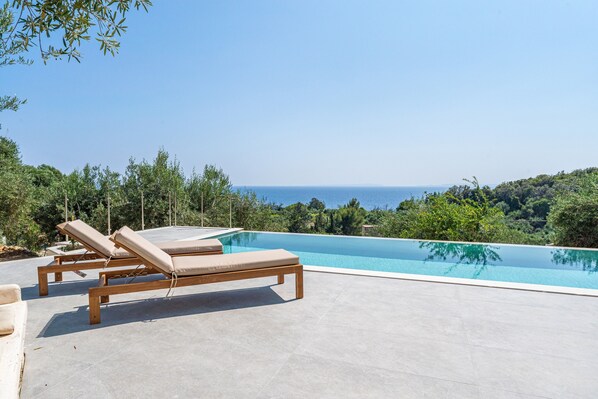 Une piscine entourée de chaises longues, de verdure et offrant une vue sur la mer.