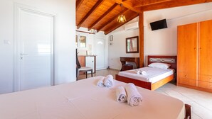 Une chambre d’hôtel avec un plafond en bois, un lit avec des serviettes roulées, un bureau, une chaise, une armoire et un téléviseur fixé au mur.