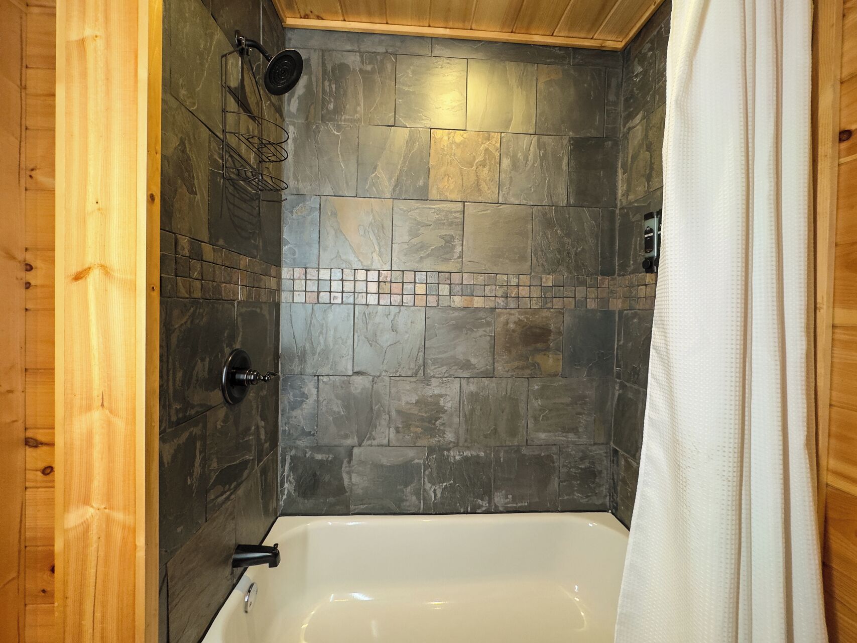 Ein Badezimmer einer Holzhütte mit einer steinverkleideten Duschwand, einer Badewanne und einem Duschkopf.