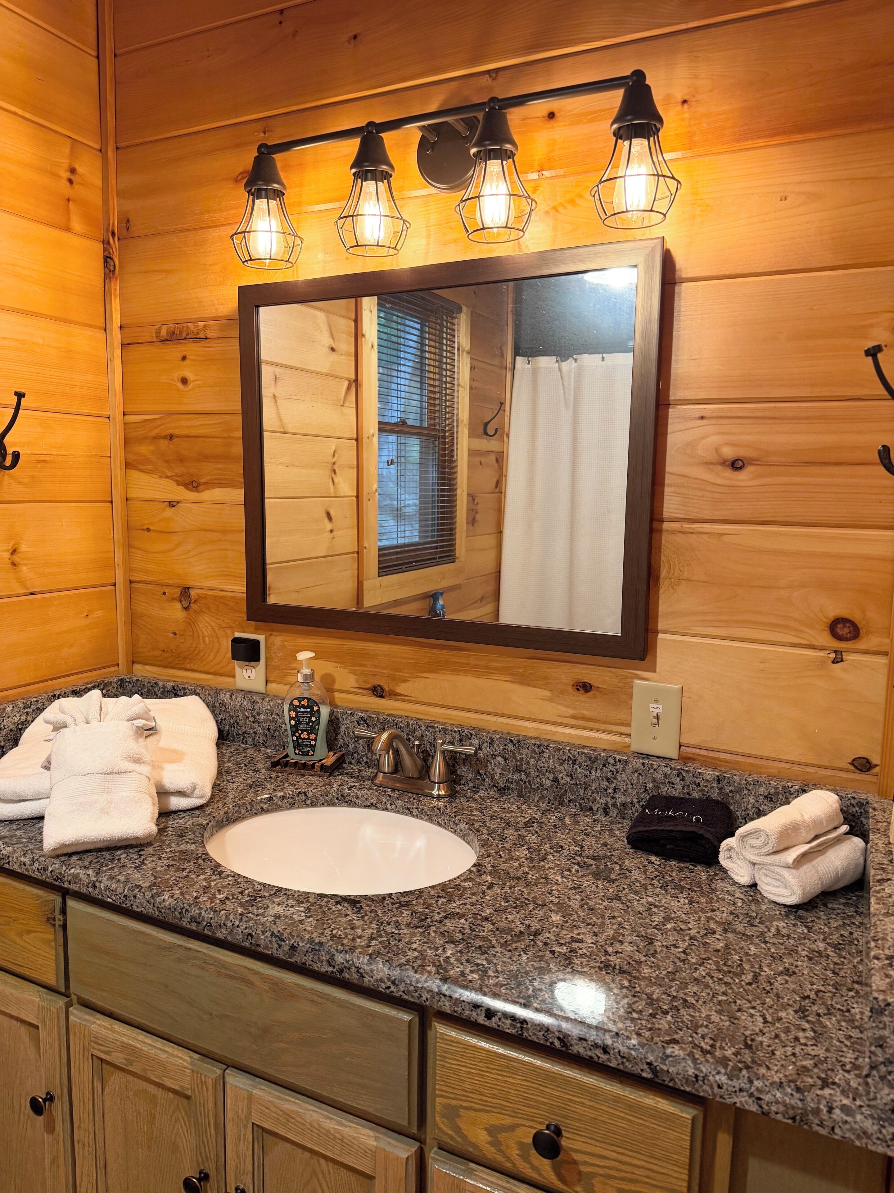 A wooden cabin-style bathroom with a granite countertop, a white sink, a mirror with lights, and towels.