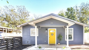 A small, single-story building with a yellow door, numbered 208, and a porch with a potted plant. - Cozy Oasis in San Marcos TX, Modern, Pet Friendly, convenient Location, Sleeps 8 (San Marcos)