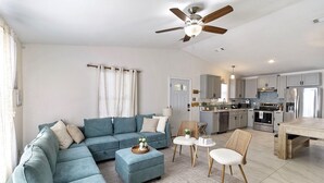 A modern living room with a sectional sofa, ottoman, and a dining area with a table and chairs. - Cozy Oasis in San Marcos TX, Modern, Pet Friendly, convenient Location, Sleeps 8 (San Marcos)