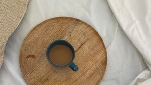 Een rond houten dienblad met een blauwe mok met een drankje, op een witte spreidek.