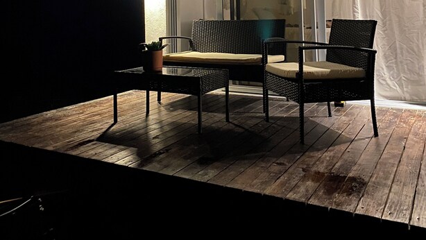 Een terras buiten met houten vloer, twee rieten stoelen, een bijzettafeltje en een potplant.