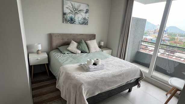 Ein Schlafzimmer mit Bett, Nachttischen, einem Fenster mit Blick und einer Deckenleuchte.