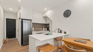 A modern kitchen with white cabinetry, a stainless steel refrigerator, a sink, and a wooden dining table with chairs.