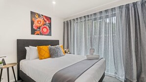 A modern bedroom with a large bed, grey curtains, and a floral painting on the wall.