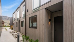 A modern building with a wooden facade, a visible door, and a small garden area with plants.