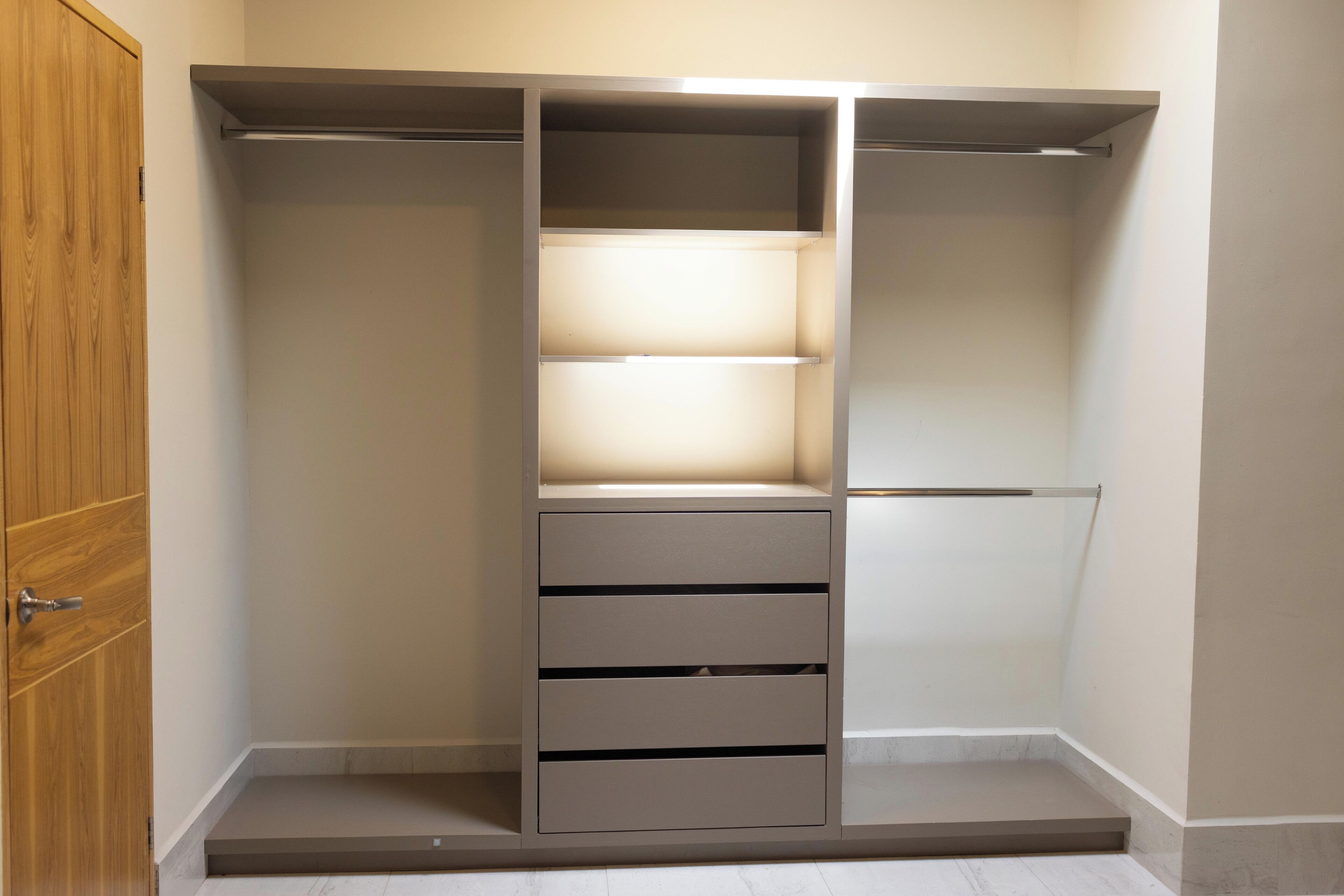 A walk-in closet with a wooden door, a lighted shelf, and a shoe rack.