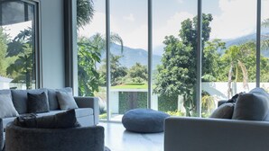 A modern living room with a large window offering a view of a lush garden and mountains. - Luxurious Getaway w Private Pool Garden (Santiago)
