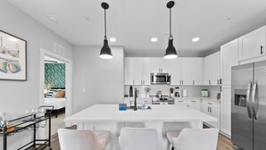 Een moderne keuken met een centraal eiland, witte kastjes, roestvrijstalen apparatuur en hanglampen.