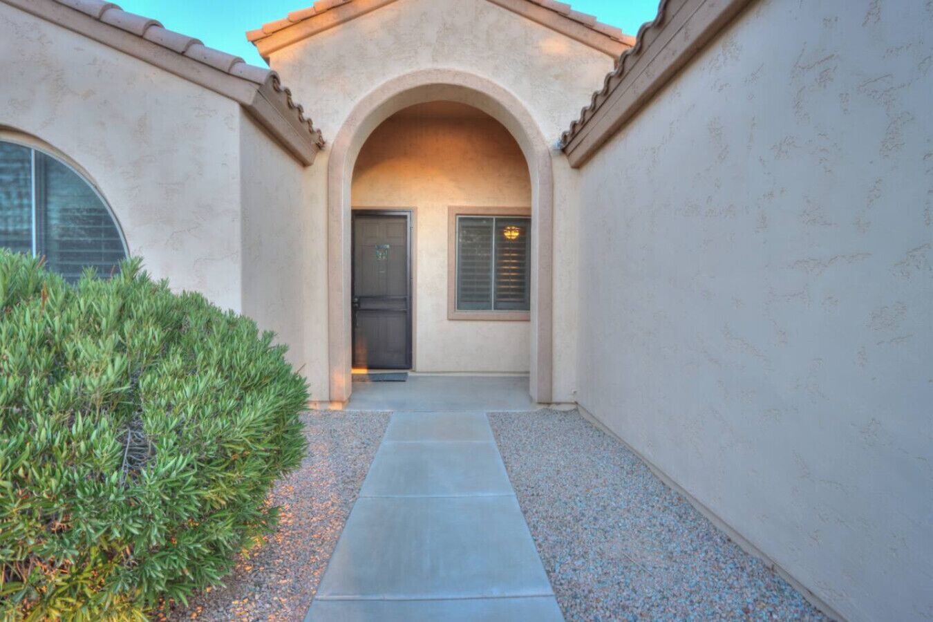 A modern building with a concrete facade, an arched entrance, and a gravel pathway leading to a door with a window.