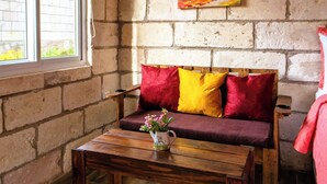 Una habitación acogedora con un banco de madera, una pequeña mesa con un florero y un cuadro de un árbol en la pared de ladrillo.