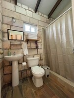 Un baño con pared de piedra, un lavabo, un inodoro y una cortina de ducha.