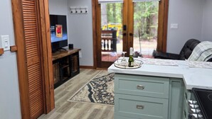 A kitchen with a wooden ceiling, a dining area with a table and chairs, and a view through a glass door to the outside. - Charming cabin in outside lovely coombs  on 10 acreas  veryprivate  (Qualicum Beach)
