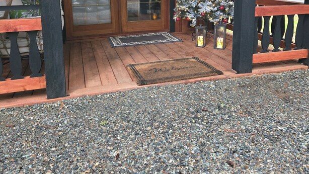 A wooden cabin entrance with a gravel driveway, a Christmas tree, and a welcome mat. - Charming cabin in outside lovely coombs  on 10 acreas  veryprivate  (Qualicum Beach)