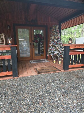 Entrada d'una cabana de fusta amb un camí de grava, un arbre de Nadal i un estora de benvinguda.