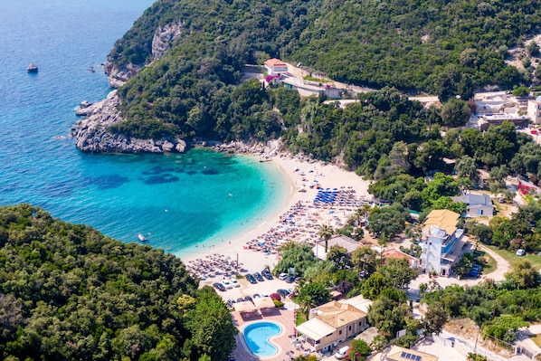 Luftaufnahme einer Küstenlandschaft mit Strand, Schwimmbecken und umgebenden Gebäuden.