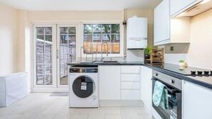 A modern kitchen with a built-in washer and dryer, white cabinetry, and a large window providing a view of the outside.