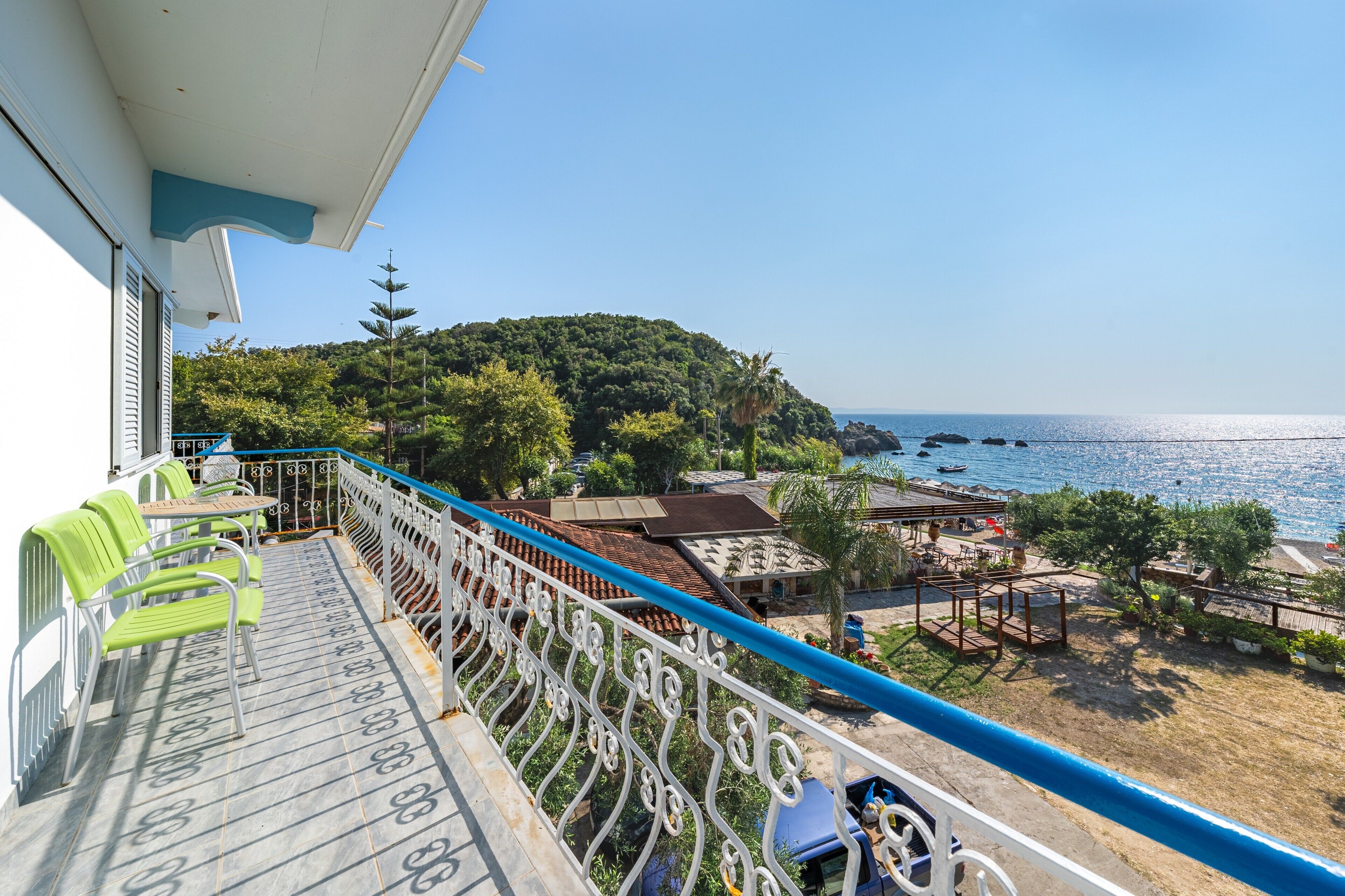 A balcony with green chairs, a railing, and a view of the sea and a hillside.